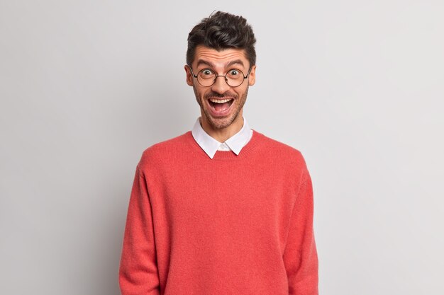 Portrait de bel homme réagit joyeusement sur quelque chose de positif regarde volontiers l'appareil photo