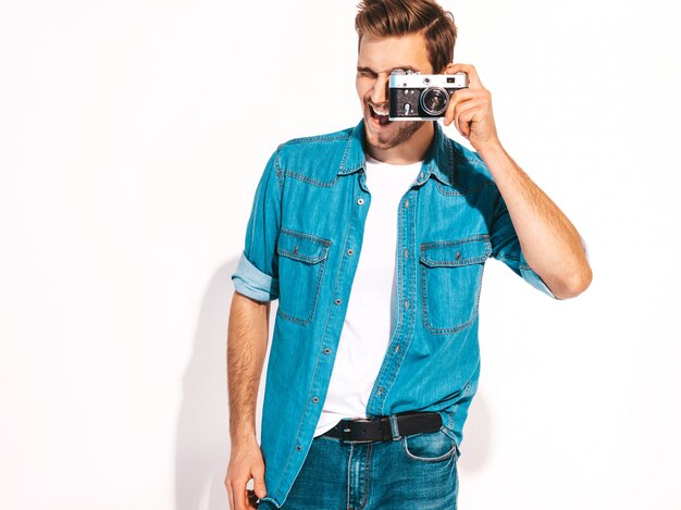 Portrait de bel homme souriant portant des vêtements de jeans d'été. Modèle masculin prenant une photo sur un ancien appareil photo vintage.