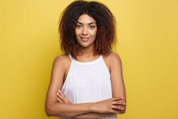 Portrait de la belle belle femme afro-américaine posant les bras croisés avec un sourire heureux. Fond d&#39;écran jaune. Espace de copie.