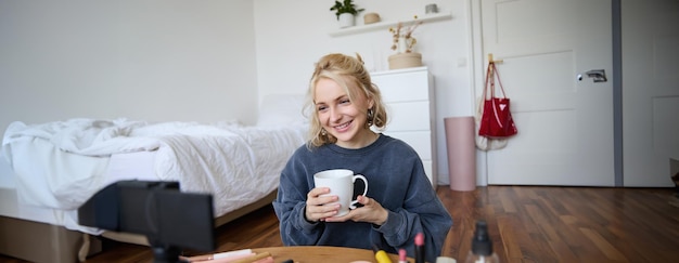 Portrait d'une belle blogueuse de beauté sur les réseaux sociaux assise devant une caméra numérique sur le sol à