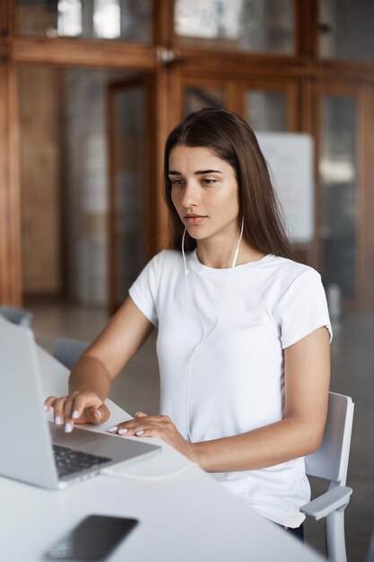 Portrait d'une belle dame étudiant à l'aide d'un ordinateur portable et d'un casque apprenant une nouvelle langue dans une bibliothèque publique Concept d'éducation