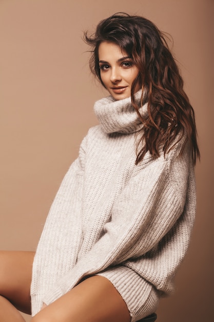 portrait de belle douce femme brune souriante mignonne. Fille en pull gris décontracté. Modèle qui pose en studio. Assis sur une chaise