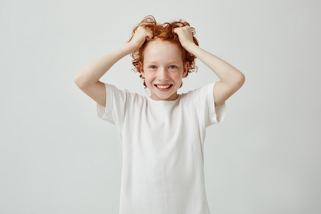 Portrait de la belle enfant tête rouge avec des taches de rousseur souriant brillamment avec des dents, tenant les cheveux dans les mains et à la recherche