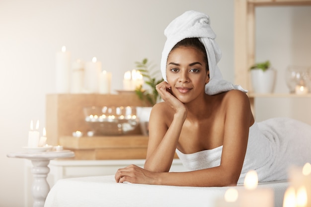Portrait de la belle femme africaine avec une serviette sur la tête en souriant au repos dans le salon spa.