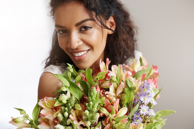 Portrait de la belle femme africaine souriante tenant le bouquet d'alstroemerias.