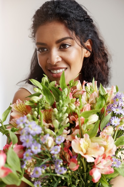 Portrait de la belle femme africaine souriante tenant le bouquet d'alstroemerias.