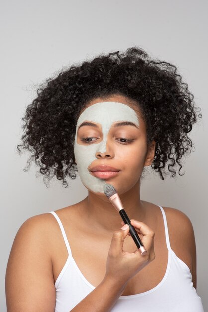 Portrait d'une belle femme appliquant un masque facial avec un pinceau de maquillage sur son visage