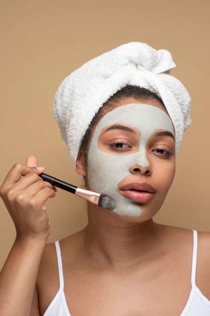 Portrait d'une belle femme appliquant un masque facial avec un pinceau de maquillage sur son visage