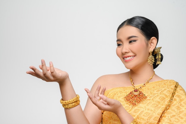 Portrait Belle femme asiatique en costume traditionnel thaïlandais souriant et pose la paume ouverte avec gracieusement sur le mur blanc