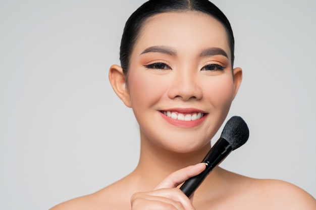 Portrait d'une belle femme asiatique tenant un pinceau à fard à joues
