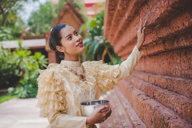 Portrait belle femme au festival de Songkran avec costume traditionnel thaïlandais dans le temple tenant un bol d'eau et sourire culture thaïlandaise avec festival de l'eau