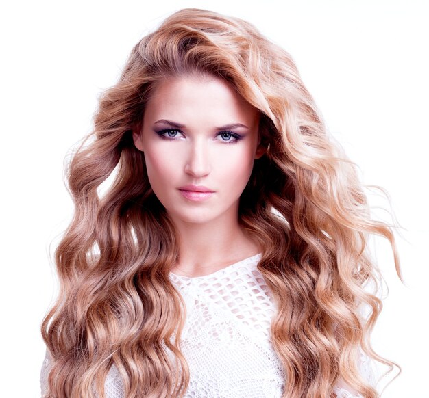 Portrait de la belle femme aux longs cheveux bouclés blonds. Mannequin posant sur un mur blanc.