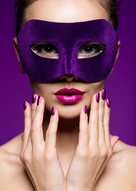 Portrait d'une belle femme aux ongles violets et masque de théâtre sur le visage.