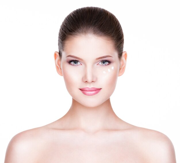 Portrait de belle femme en bonne santé avec une crème cosmétique sous les yeux - isolé sur blanc.