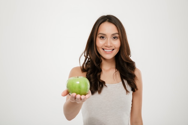 Portrait de belle femme en bonne santé souriant et montrant la pomme juteuse verte à la caméra, isolé sur blanc