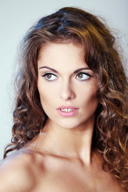 Portrait d'une belle femme brune aux cheveux bouclés et épaules nues posant sur un fond clair