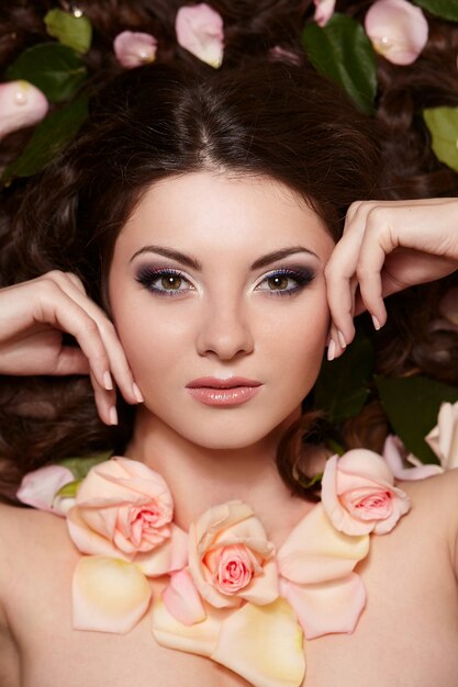 Portrait de la belle femme brune aux longs cheveux bouclés et maquillage lumineux avec des fleurs dans les cheveux