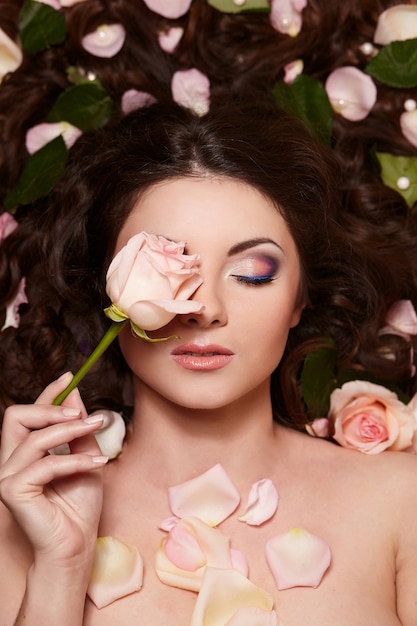 Portrait de la belle femme brune aux longs cheveux bouclés et maquillage lumineux avec des fleurs dans les cheveux