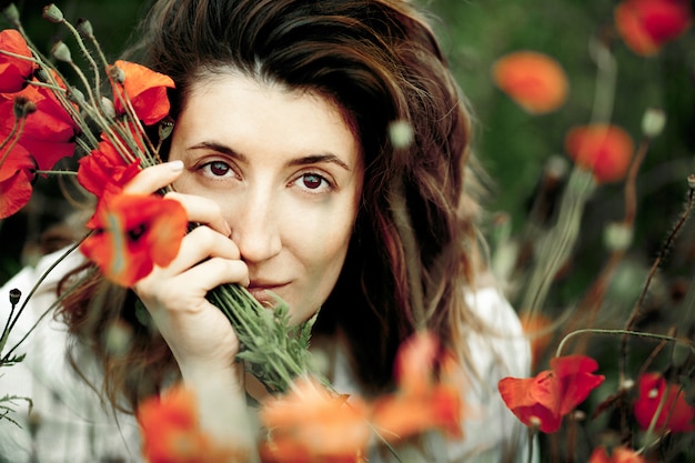 Portrait de la belle femme brune avec le bouquet de fleurs de coquelicots