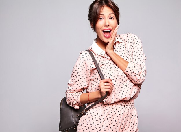 Portrait de la belle femme brune mignonne surprise modèle dans des vêtements d'été décontractés sans maquillage isolé sur un mur gris avec sac à main