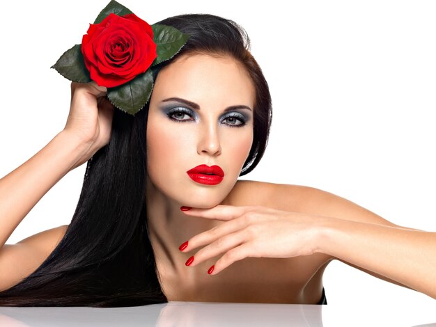 Portrait d'une belle femme brune avec des ongles rouges et des lèvres tient la rose rouge