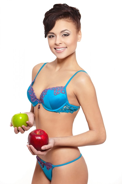 Portrait de la belle femme brune souriante en lingerie blanche avec un régime de pomme verte et rouge isolé sur blanc