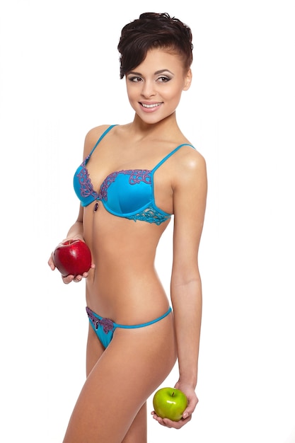 Portrait de la belle femme brune souriante en lingerie blanche avec un régime de pomme verte et rouge isolé sur blanc