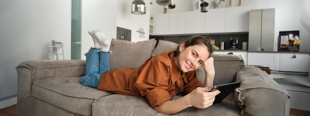 Portrait d'une belle femme brune souriante passant du temps à la maison en utilisant une tablette numérique allongée sur