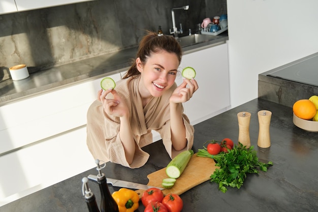 Portrait d'une belle femme cuisinant de la salade dans la cuisine, coupant des légumes et souriant en préparant