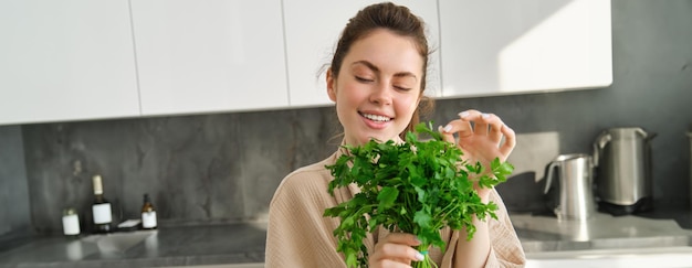 Photo gratuite portrait d'une belle femme cuisinant tenant du persil frais en ajoutant des herbes tout en préparant une salade saine