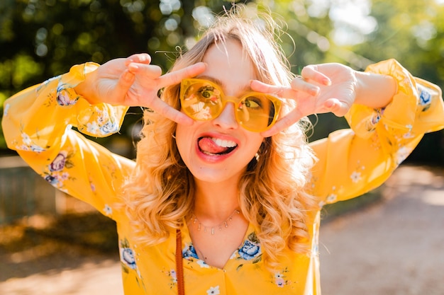 Portrait de la belle femme émotionnelle élégante blonde en chemisier jaune portant des lunettes de soleil, drôle d'expression du visage fou