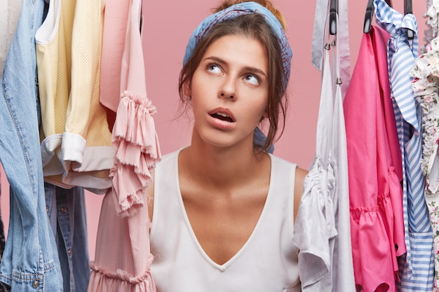 Portrait de belle femme avec une expression fatiguée, regardant à travers un étagère de vêtements, faire du shopping le week-end, être épuisée de mettre des vêtements, vouloir se reposer à la maison. Acheteuse occupée