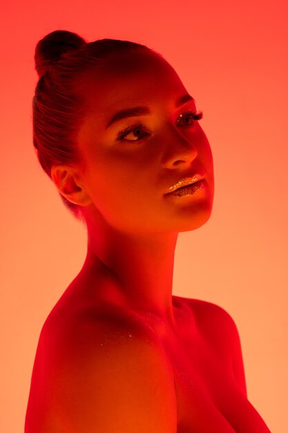 Portrait de belle femme isolé sur fond de studio rouge-orange en néon, monochrome. Beau modèle féminin. Concept d'émotions humaines, expression faciale, ventes, publicité, mode et beauté.