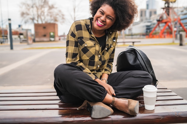 Portrait de la belle femme latine afro-américaine assise avec une tasse de café à l'extérieur dans la rue. Concept urbain.