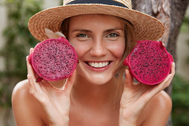 Portrait de belle femme avec un look attrayant, porte un chapeau d'été de paille, détient des fruits du dragon