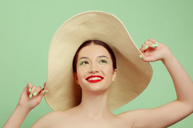 Portrait de belle femme avec maquillage lumineux et chapeau sur studio vert