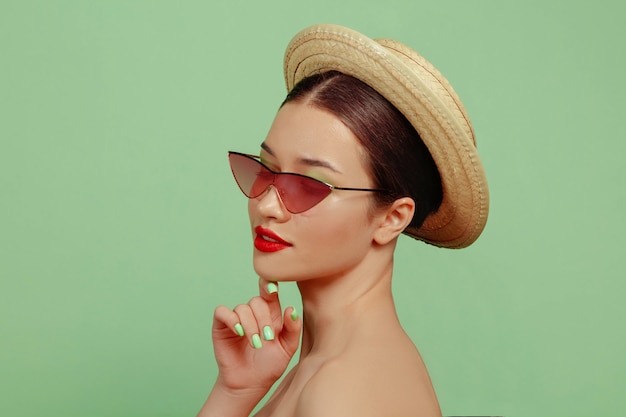 Portrait De Belle Femme Avec Maquillage Lumineux, Lunettes Rouges Et Chapeau. Marque Et Coiffure élégantes Et à La Mode. Couleurs De L'été. Posant.