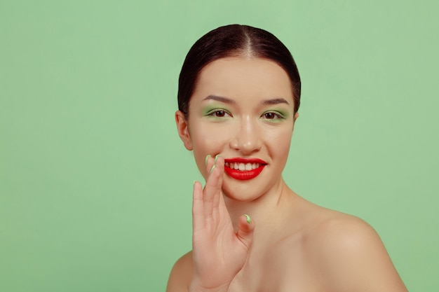 Photo gratuite portrait de belle femme avec maquillage lumineux, lunettes rouges et chapeau sur studio vert