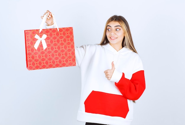 Portrait de belle femme modèle debout avec un sac cadeau et montrant le pouce vers le haut