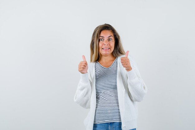 Portrait de belle femme montrant les pouces vers le haut en veste et à la vue de face heureux