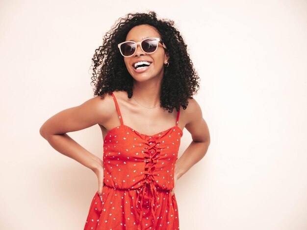 Portrait de belle femme noire avec une coiffure de boucles afro Modèle souriant vêtu d'une robe d'été rouge Sexy femme insouciante mur blanc isolé en studio