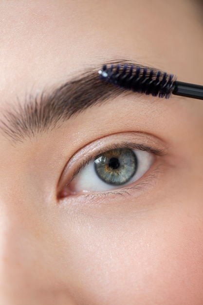 Portrait d'une belle femme à la peau claire à l'aide d'une brosse pour ses sourcils