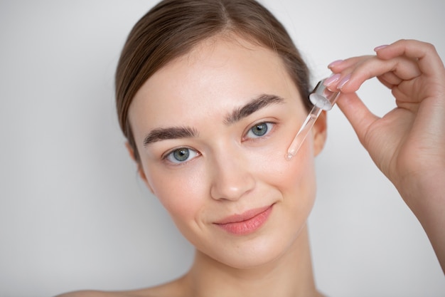 Portrait d'une belle femme à la peau claire à l'aide d'un sérum pour le visage