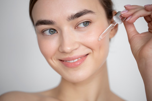 Photo gratuite portrait d'une belle femme à la peau claire à l'aide d'un sérum pour le visage