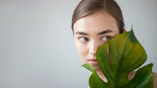 Portrait d'une belle femme à la peau claire posant avec une feuille de plante monstre