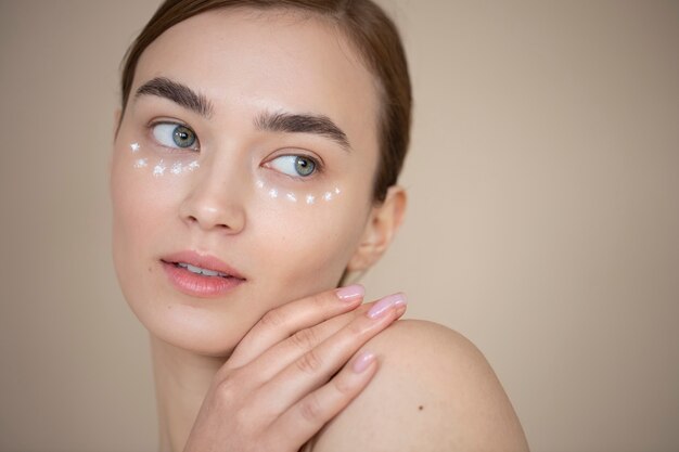 Portrait d'une belle femme à la peau claire utilisant une crème pour les yeux