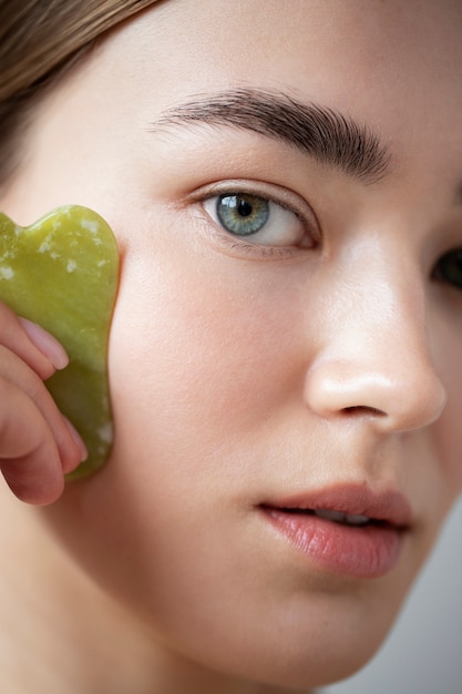 Portrait d'une belle femme à la peau claire utilisant du guasha pour masser son visage