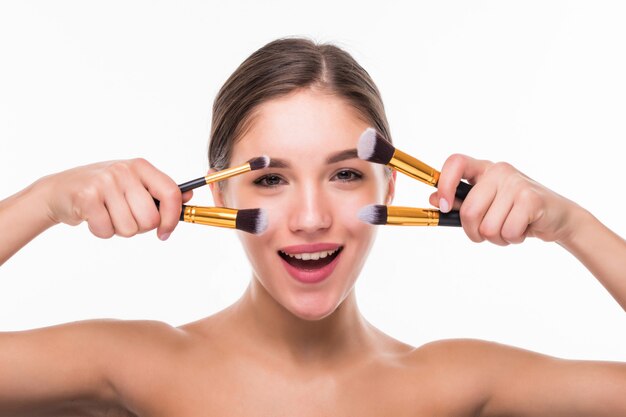 Portrait de la belle femme avec des pinceaux à maquillage près de visage attrayant sur mur blanc