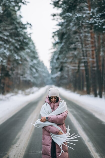 Portrait d'une belle femme de race blanche sur une route à travers la forêt enneigée