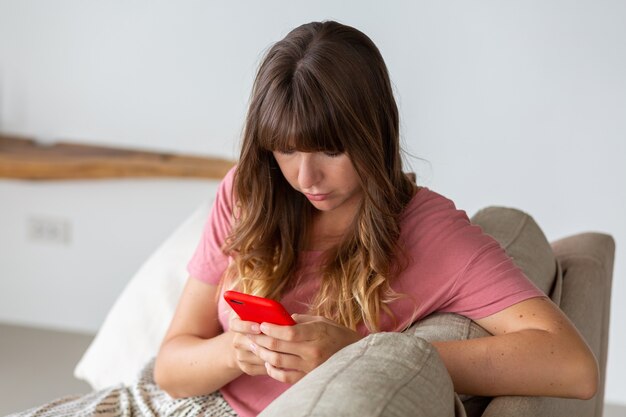 Portrait de la belle femme reposante sur le canapé à la maison. Femme tenant dans sa main un téléphone intelligent.